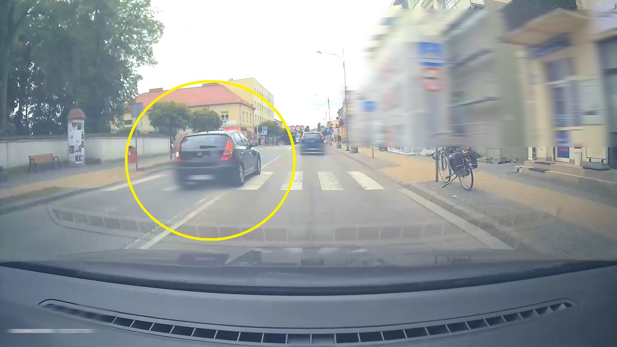 Osobowe auto wyprzedza pod prąd pojazdy na przejściu dla pieszych.