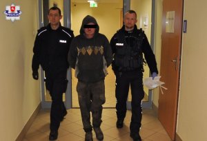 Zatrzymany mężczyzna z kapturem na głowie prowadzony przez policjantów