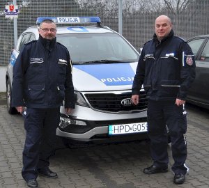 Policjanci wykonujący eskortę do szpitala przy radiowozie