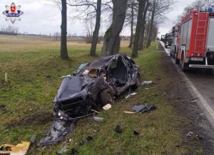 Rozbity samochód osobowy stoi w rowie, po prawej stronie stai samochód straży pożarnej