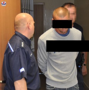 Mężczyzna w szarej bluzie prowadzony przez policjantów