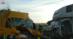 Uszkodzone samochody typu bus stoją na jezdni. Przed nim laweta.