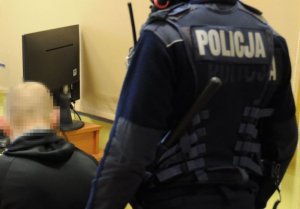 Zatrzymany mężczyzna siedzi na krześle w asyście policjantów