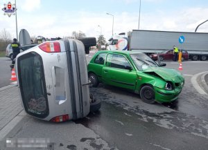 samochód opel zafira wywrócony na lewy bok , obok nissan micra z rozbitym przodem w tle trasa k19, i policjant który kieruje ruchem.