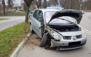 Uszkodzony samochód stoi na jezdni. Za nim radiowóz oznakowany