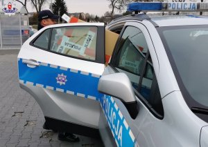 Policjant wyjmuje z radiowozu paczkę