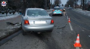 Rozbity samochód audi stoi na jezdni. Przed nim oznakowany radiowóz policyjny