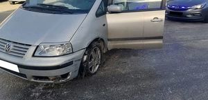 Samochód marki VW Sharan stoi na parkingu. Za nim nieoznakowany radiowóz z włączonymi światłami błyskowymi