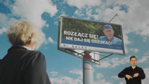 Zdjęcie przedstawia starszą kobietę patrzącą w bilbord na którym jest inny starszy mężczyzna i napis: Rozłącz się nie daj się oszukać!