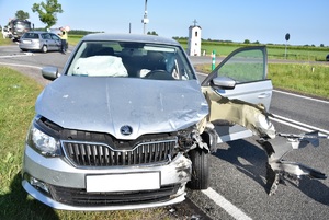 Uszkodzony samochód marki Skoda stoi na jezdni za nim policjant wykonuje czynności na miejscu zdarzenia.