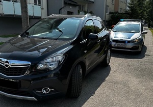 Samochód marki Opel Mokka stoi na jezdni, a za nim oznakowany radiowóz policyjny