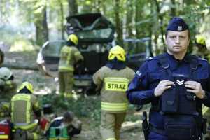 policjant zabezpiecza miejsce zdarzenia. W tle strażacy