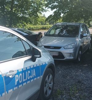 Ford C-Max stoi na parkingu, a przed nim oznakowany radiowóz