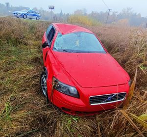 Uszkodzony samochód marki Volvo stoi na łące. Za nim na drodze oznakowany radiowóz