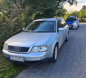 Samochód marki Audi stoi na jezdni, a za nim oznakowany radiowóz