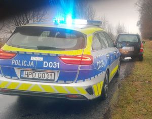Opel Astra stoi na jezdni,a za nim oznakowany radiowóz policyjny