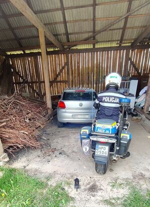 VW zaparkowany w stodole. Za nim stoi policjant na motocyklu